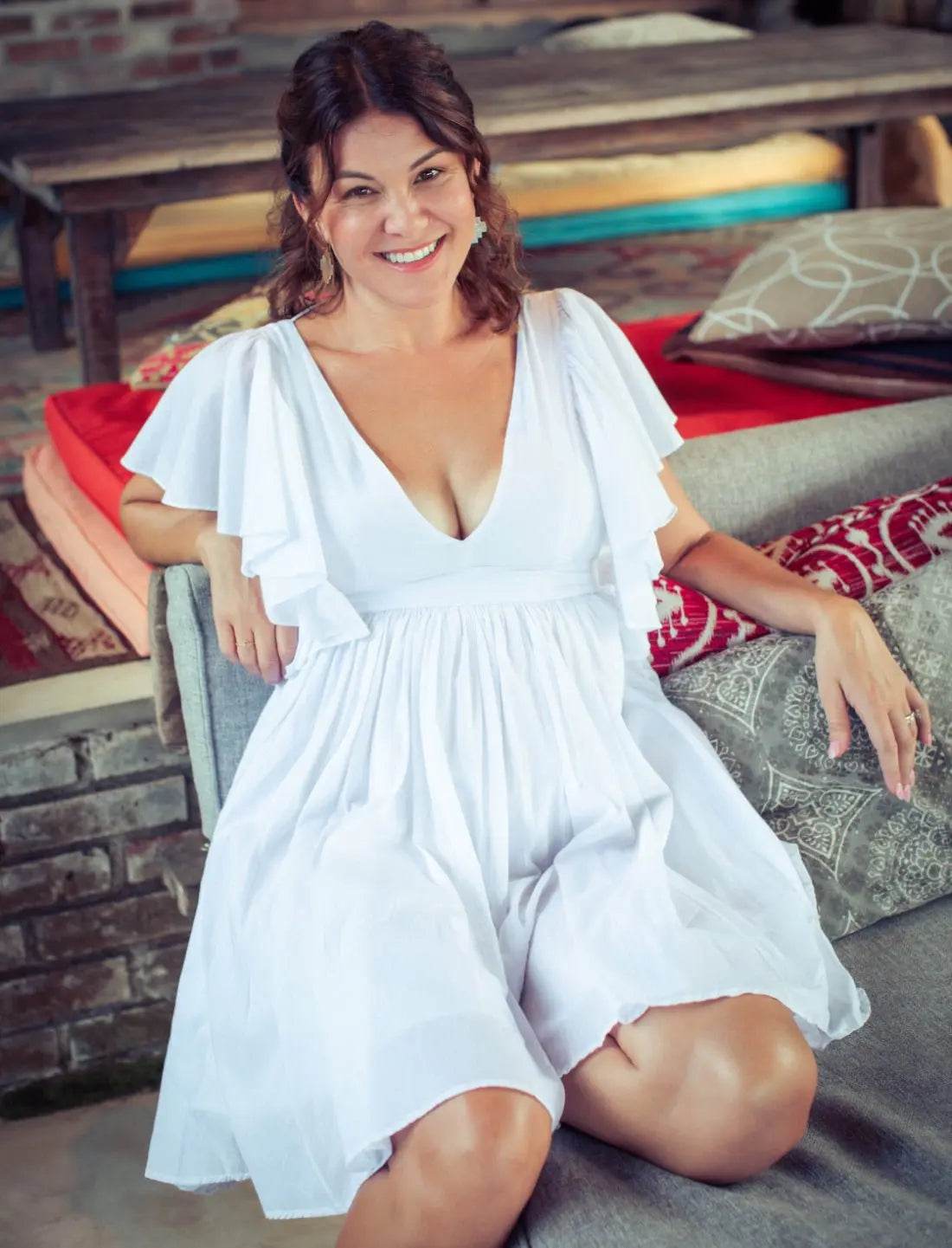 Playful Ina Short Dress in crisp white with flutter sleeves and v-neckline, perfect for summer beach weddings and resort wear. Lightweight cotton dress featuring feminine silhouette, flowy gathered skirt, and comfortable fit. Ethical fashion, sustainable clothing, vacation outfit, bridal shower dress, honeymoon attire, casual wedding dress, bohemian style, handcrafted apparel photographed in rustic beach lounge setting.