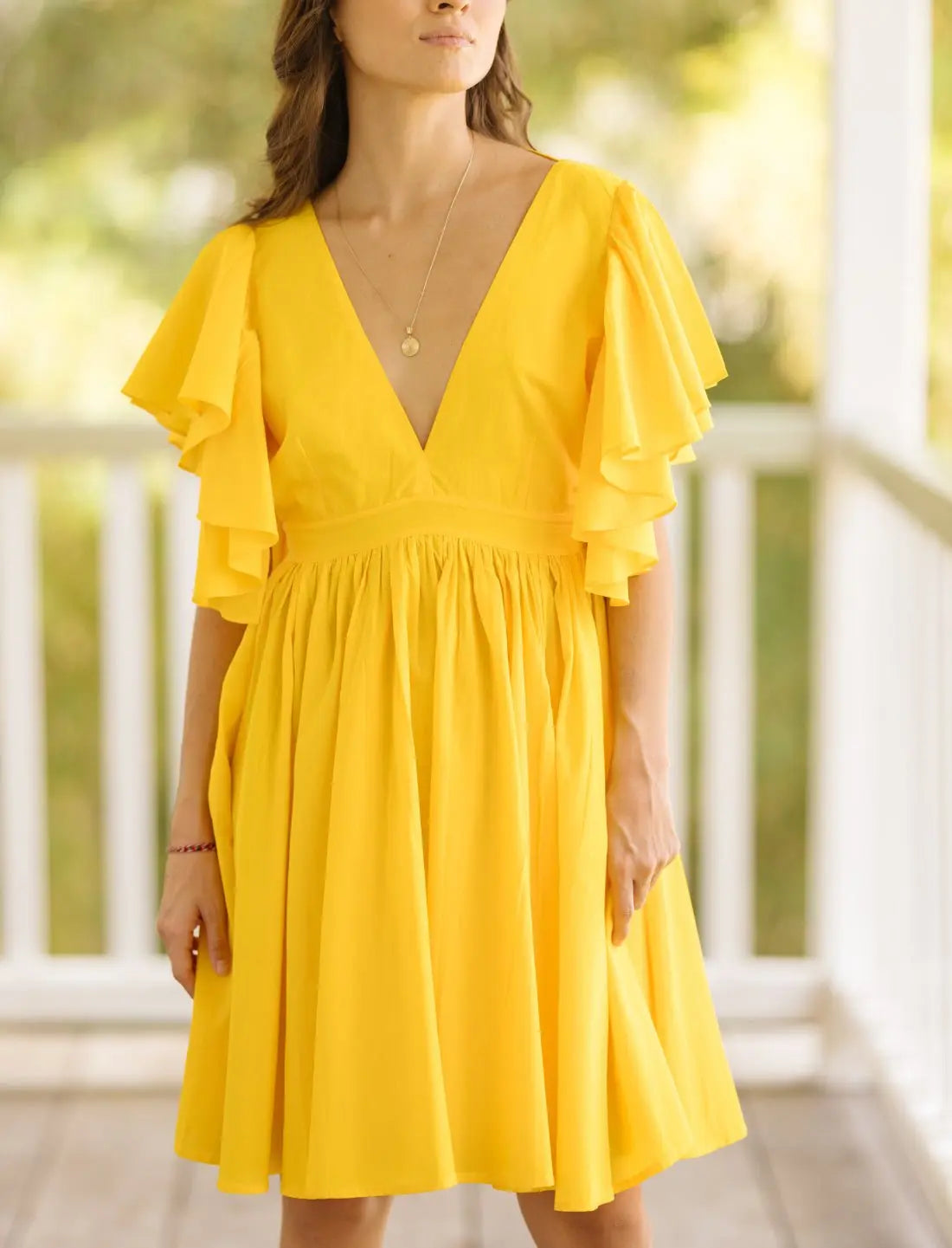 Playful Ina Short Dress in bright sunshine yellow featuring flutter sleeves, plunging v-neckline and gathered empire waist. Summer wedding guest dress, ethical fashion, sustainable clothing, bohemian style, handcrafted apparel, bridesmaid dress, bridal shower outfit, vacation wear, beach party dress, feminine silhouette, artisan made clothing, statement color dress photographed in soft natural light.