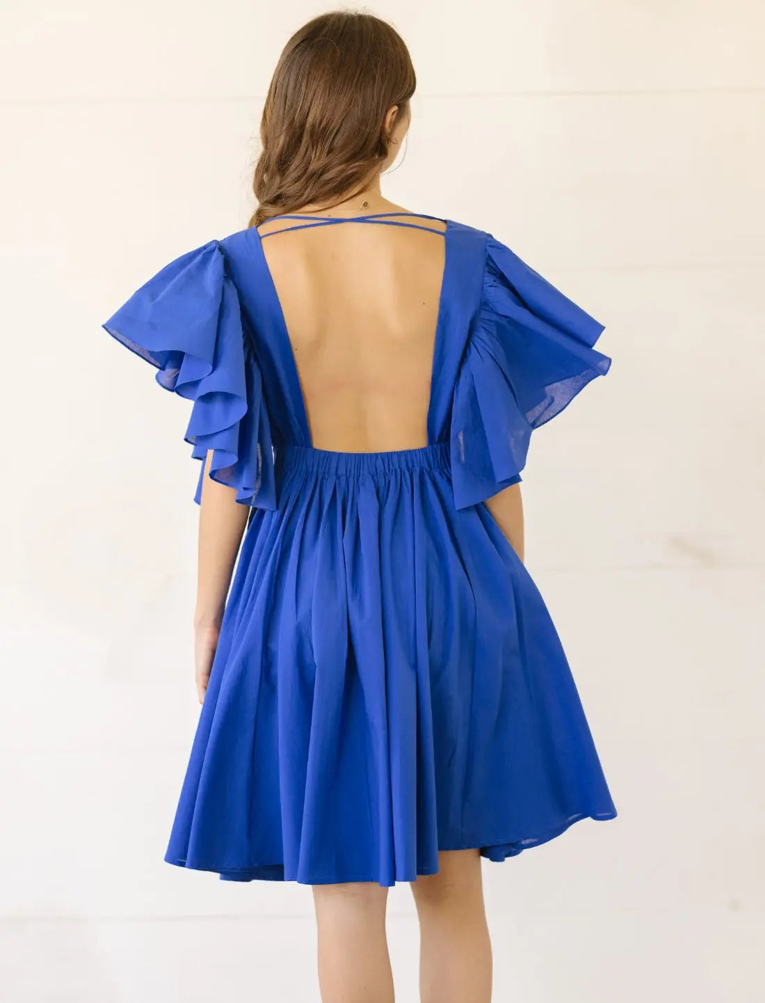 Playful Ina Short Dress in royal blue showcasing dramatic open back design with criss-cross straps and flutter sleeves. Bohemian backless dress, ethical fashion, summer cocktail attire, sustainable clothing, handcrafted apparel, wedding guest outfit, vacation dress, beach party wear, artisan made clothing, feminine flowy silhouette, special occasion dress photographed against clean white background.