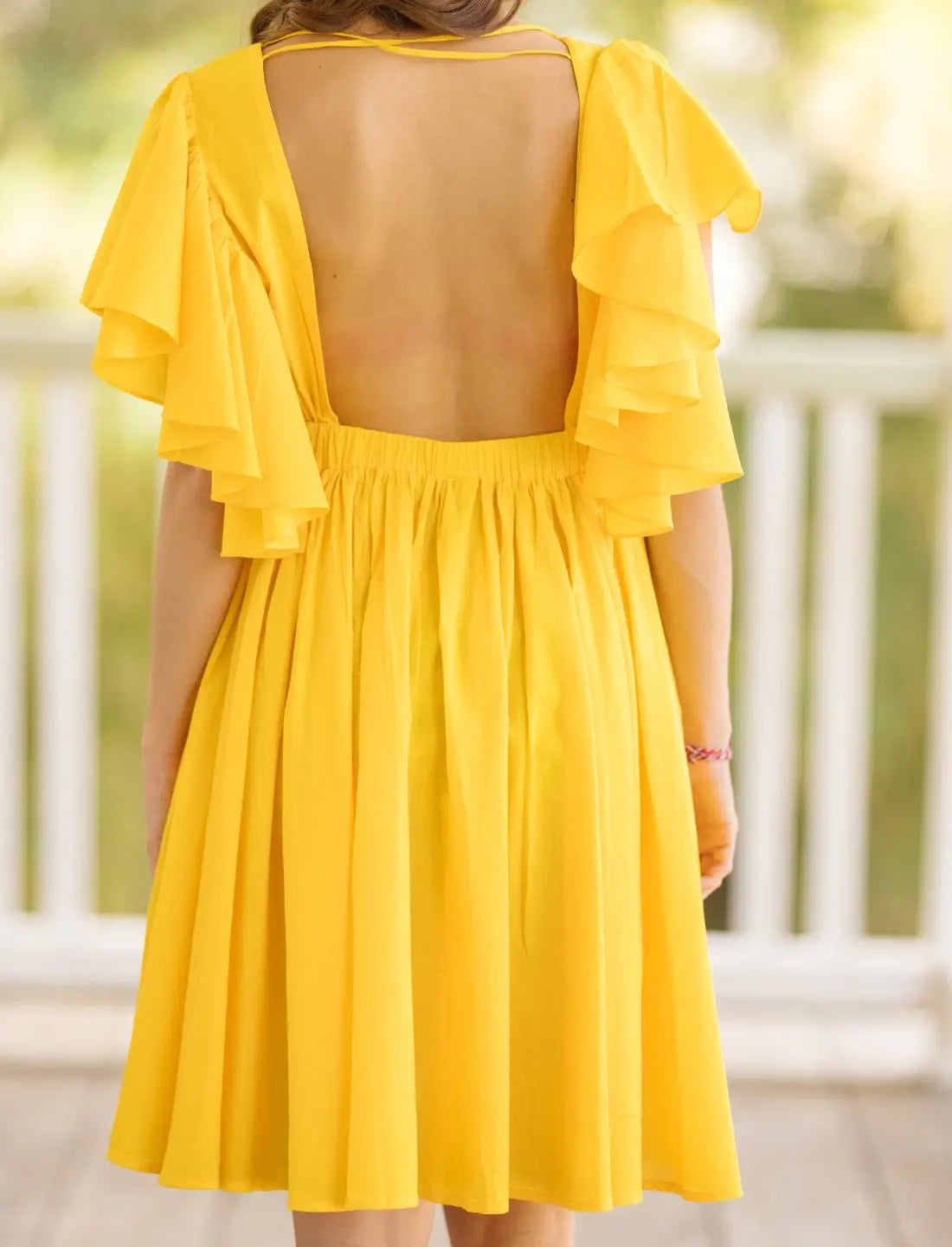Playful Ina Short Dress in vibrant yellow showcasing open back design with thin straps and cascading flutter sleeves. Bohemian summer fashion, backless dress, ethical clothing, sustainable apparel, wedding guest outfit, bridal shower dress, beach party attire, handcrafted fashion, vacation wear, feminine silhouette, garden party dress, artisan made clothing photographed in soft natural outdoor lighting.