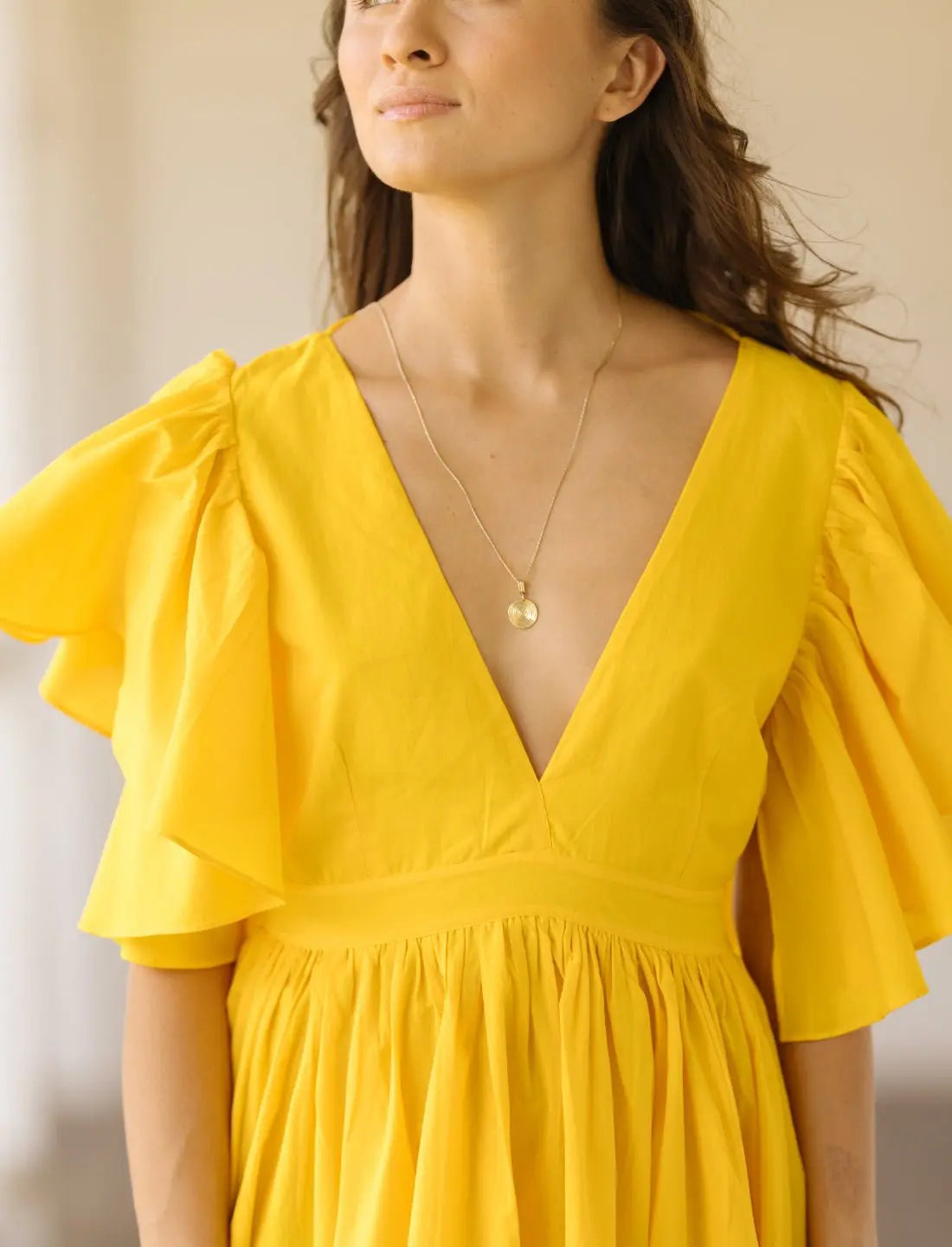 Playful Ina Short Dress in bright sunshine yellow featuring flutter sleeves, plunging v-neckline and gathered empire waist. Summer wedding guest dress, ethical fashion, sustainable clothing, bohemian style, handcrafted apparel, bridesmaid dress, bridal shower outfit, vacation wear, beach party dress, feminine silhouette, artisan made clothing, statement color dress photographed in soft natural light.