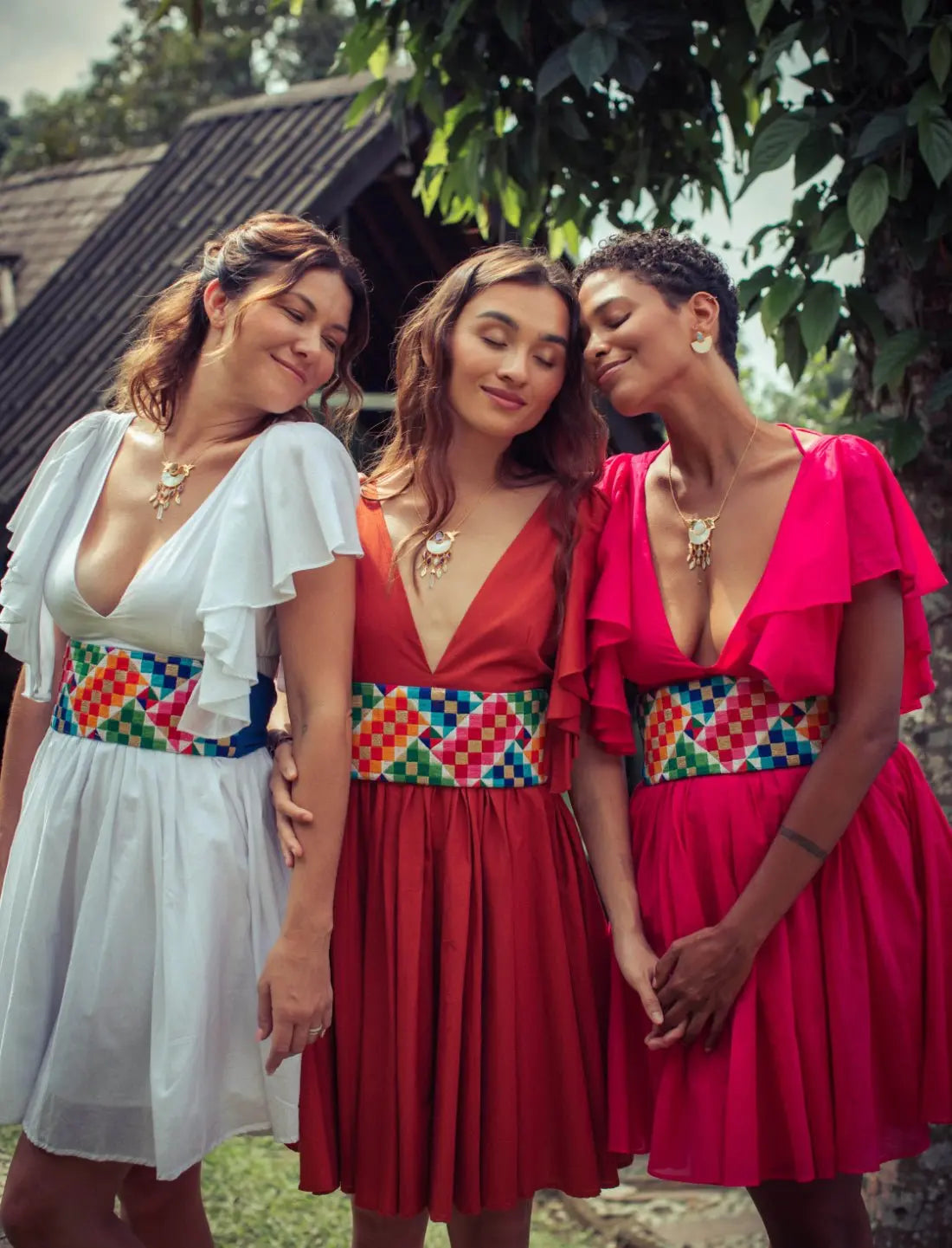 Playful Ina Short Dress collection showcased as colorful bohemian bridesmaid dresses in white, terracotta, and fuchsia with matching Rainbow Wide Belts. Ethical fashion, sustainable wedding attire, coordinated bridal party outfits, handcrafted belts with geometric patterns, destination wedding fashion, flutter sleeve design, v-neckline, artisan made clothing, beach wedding apparel, summer bridesmaid dresses, fair trade fashion photographed in tropical garden setting.