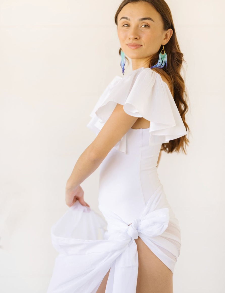 A model wearing the white Ina Bodysuit with flutter sleeves. She has styled it with a white Sash Belt tied like a sarong.