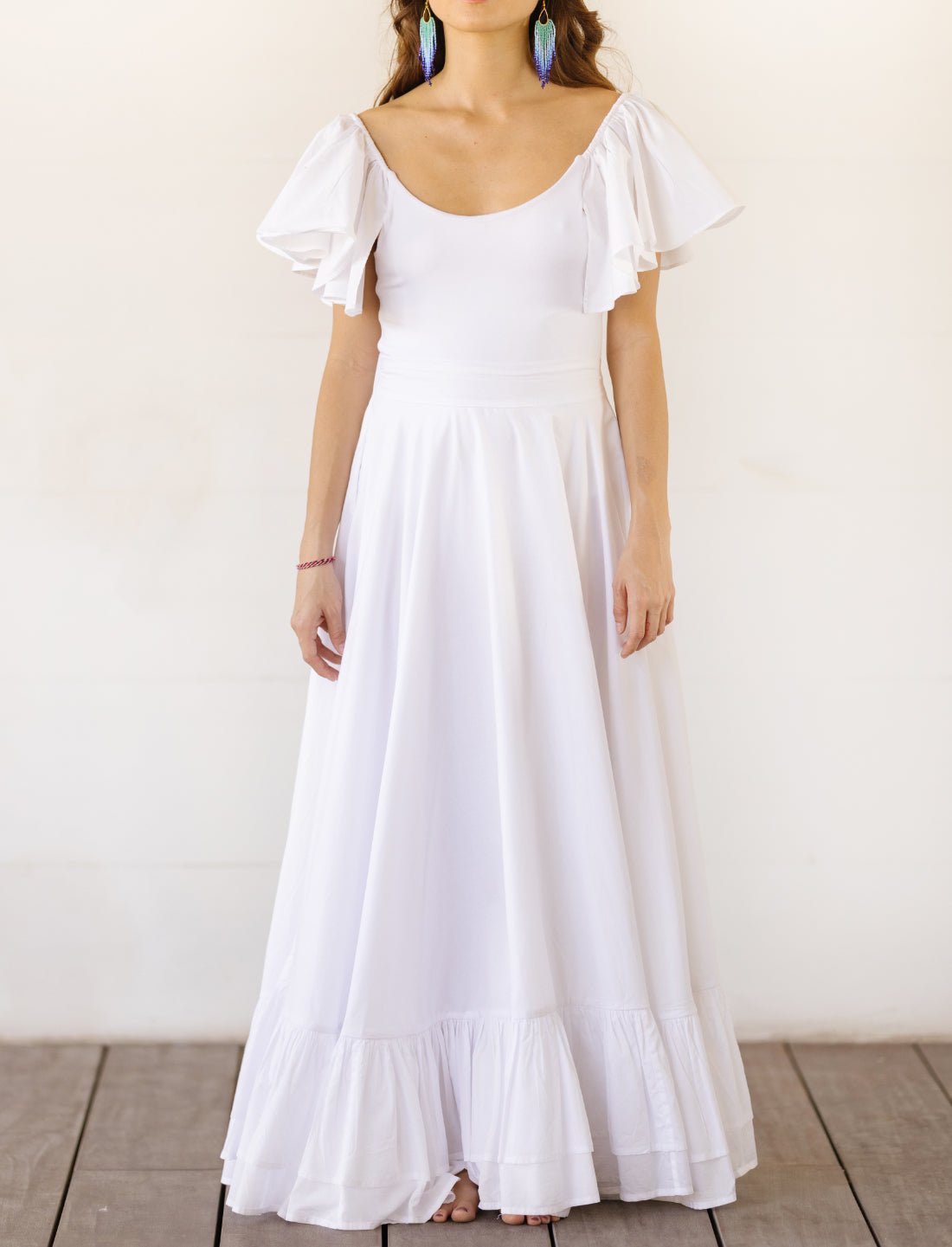 Sacred Hoop of Life Maxi Skirt in crisp white with matching flutter sleeve Ina Bodysuit top and colorful beaded statement earrings. Bohemian wedding dress, ethical fashion, sustainable clothing, beach ceremony gown, simple bridal dress, ruffle hem design, handcrafted apparel, minimalist wedding style, artisan made clothing, summer bridal attire, barefoot elegance photographed against clean white background.