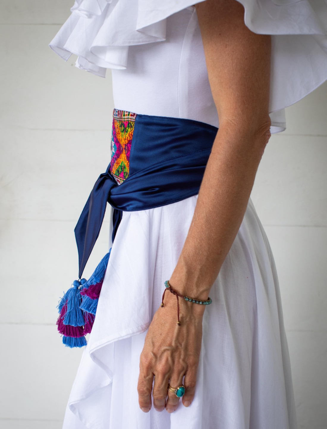 This image shows a side view of the Eye of Dharma Embroidered Belt. Here you can see how the weave pattern transitions to a pure silk sash in a royal blue color. The ends of the sash are tied back in the front, and include beautiful tassels.