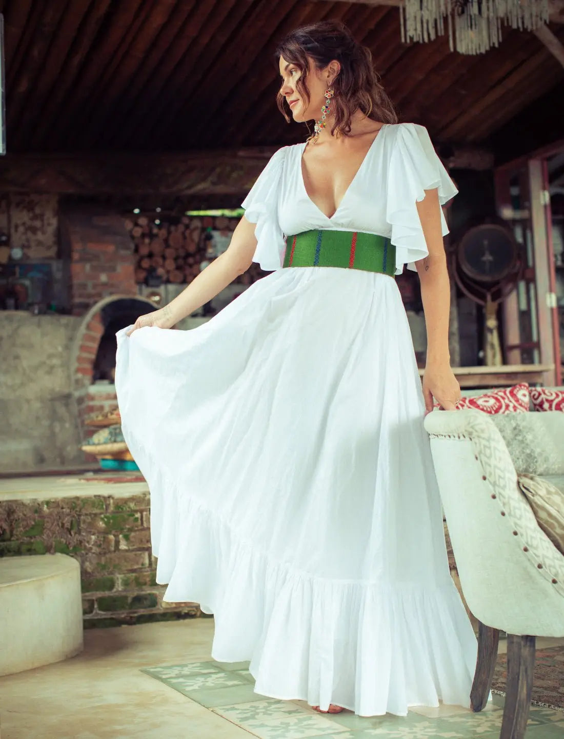 Pure white Regal Spirit Maxi Dress with flutter sleeves, deep v-neck, and long flowing skirt, modeled in a rustic jungle resort with natural light. Bohemian summer fashion, flowing silhouette, v-neck design, tiered skirt, ethical clothing, resort wear, beach vacation dress, artisan crafted details, sustainable fashion, handwoven accessories, island lifestyle, relaxed luxury, fair trade apparel.