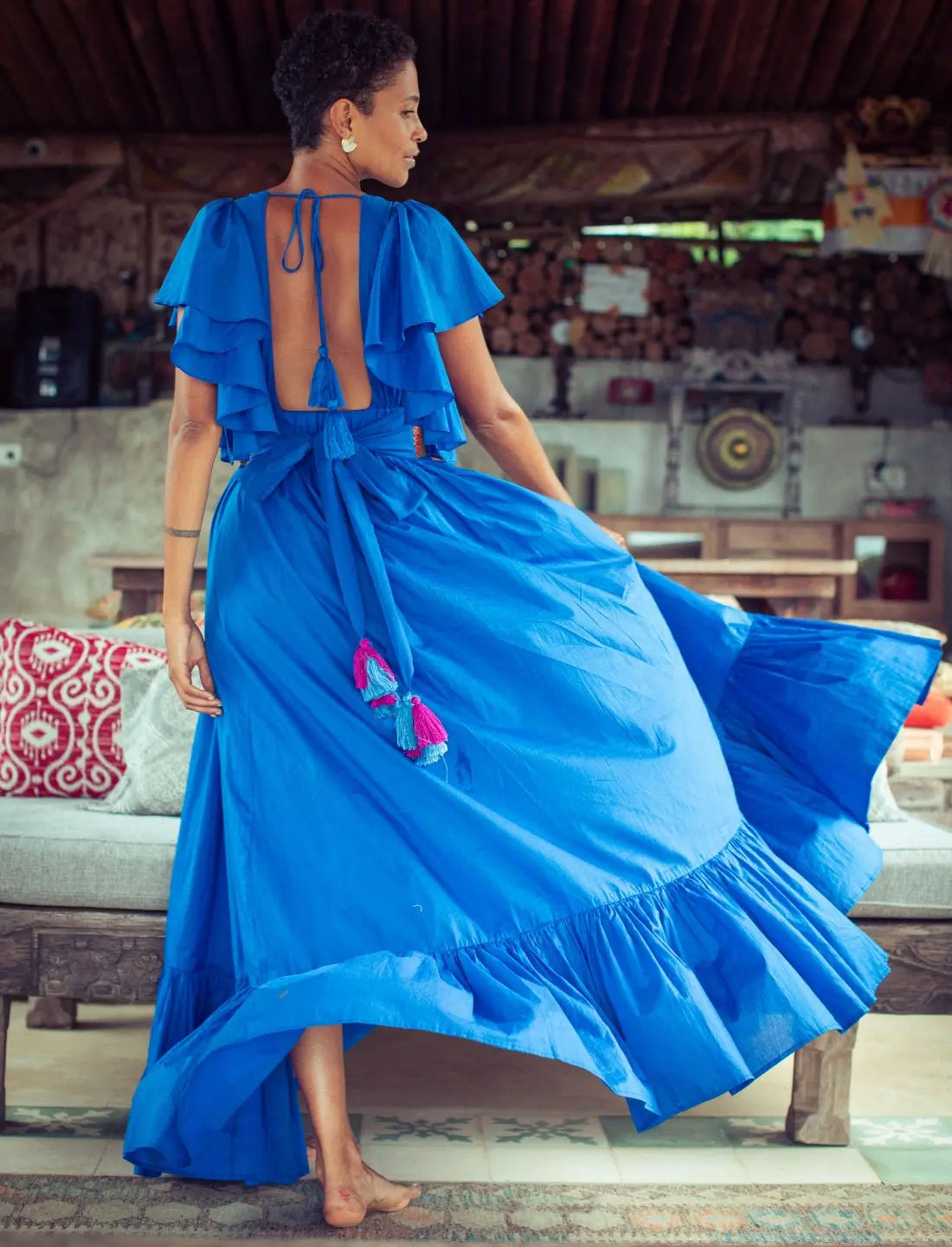 Royal blue open back Regal Spirit Maxi Dress with flutter sleeves, showcasing elegant backless design with tie closure. Bohemian resort wear, flowing tiered skirt in motion, summer destination dress, ethical fashion, handcrafted details, beach wedding guest attire, sustainable clothing, barefoot luxury, island-inspired fashion, artisan crafted apparel photographed in rustic beach lounge setting.