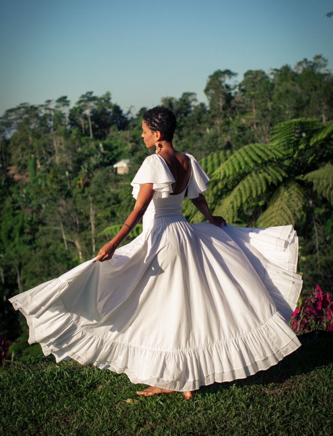 Sacred Hoop of Life Maxi Skirt in crisp white shown in motion with matching flutter sleeve top and open back design. Bohemian wedding dress, ethical fashion, sustainable clothing, bridal attire, ruffle hem design, flowing silhouette, summer resort wear, beach wedding dress, handcrafted apparel, danceable movement, artisan made clothing photographed against lush tropical jungle backdrop.