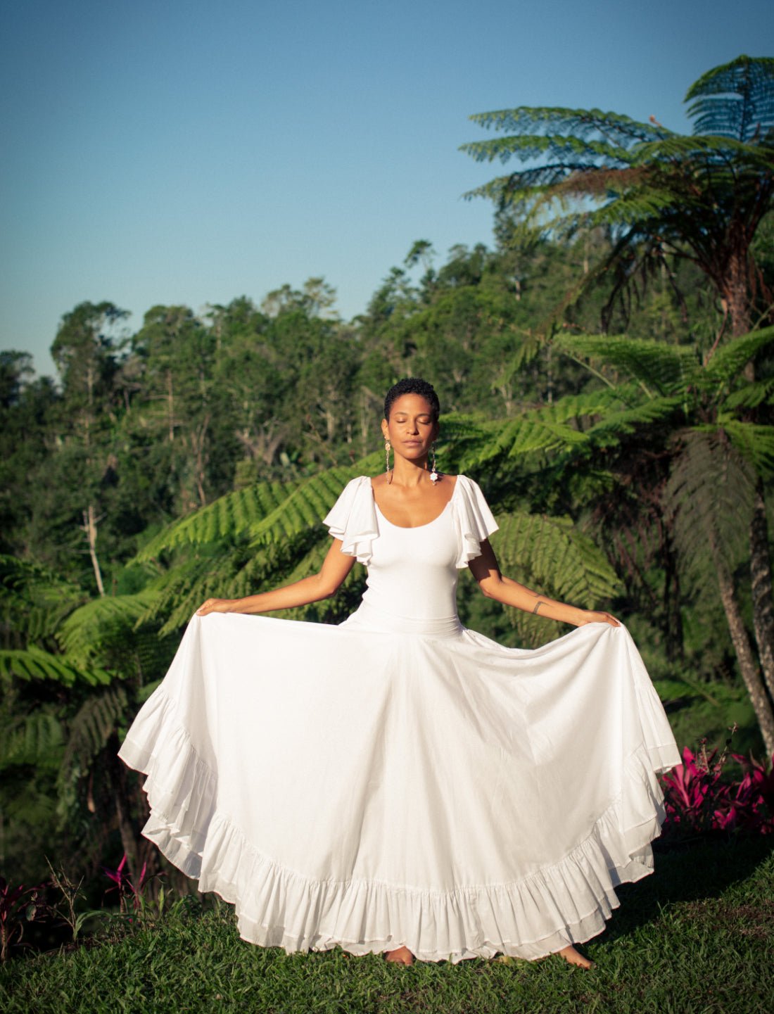 Sacred Hoop of Life Maxi Skirt in pure white with matching flutter sleeve top, displayed in full circle with ruffle hem detail. Bohemian wedding dress, ethical bridal fashion, sustainable clothing, beach ceremony gown, destination wedding attire, minimalist bridal style, handcrafted apparel, summer wedding dress, artisan made clothing, barefoot bride, natural wedding gown photographed in tropical jungle setting with fern backdrop.